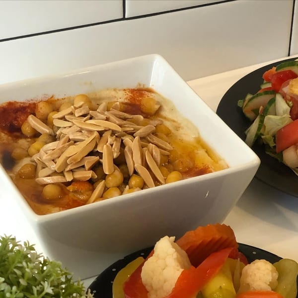 Hummus topped with chickpeas, almonds, and paprika, alongside a fresh salad and pickled vegetables.