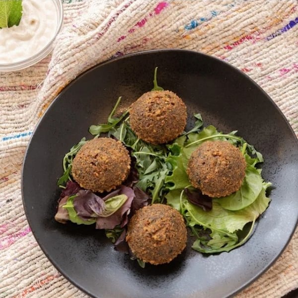 Four crispy falafel balls on a bed of mixed greens, with a side of white dipping sauce.