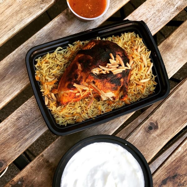 Grilled chicken with rice and almonds, with sides of red sauce and white yogurt.