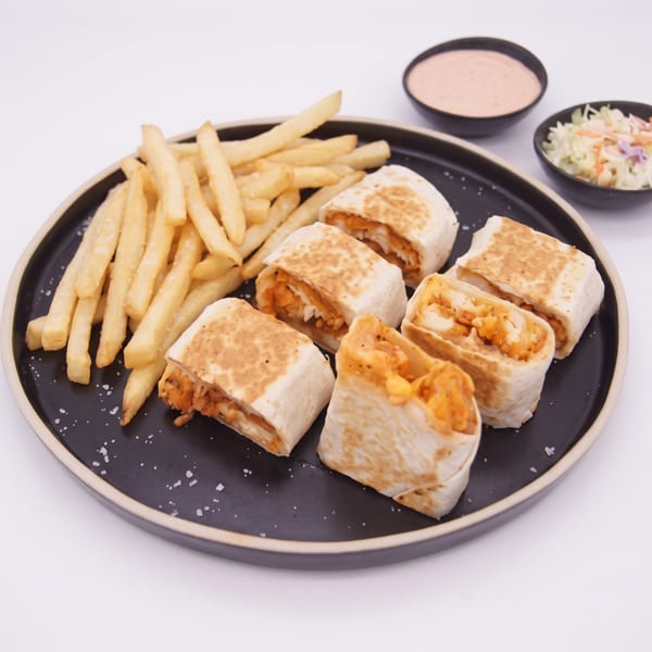A black plate with french fries, chicken wraps, coleslaw, and dipping sauce on a white background.