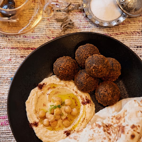 A black plate of falafel, hummus with chickpeas and olive oil, and pita bread.