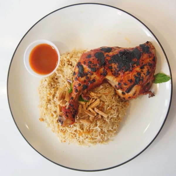 Grilled chicken leg quarter with rice, almond slivers, mint, and a side of red sauce.
