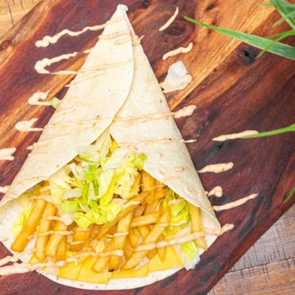 A large wrap filled with french fries, cheese, and lettuce, drizzled with sauce on a wooden board.