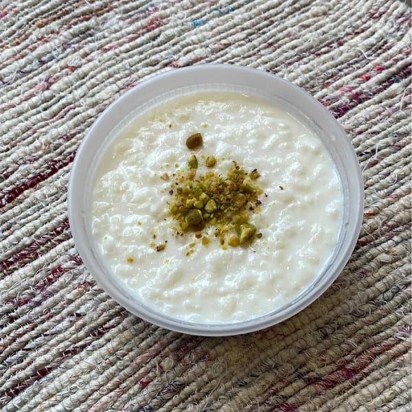 Creamy rice pudding topped with crushed pistachios in a clear plastic container.